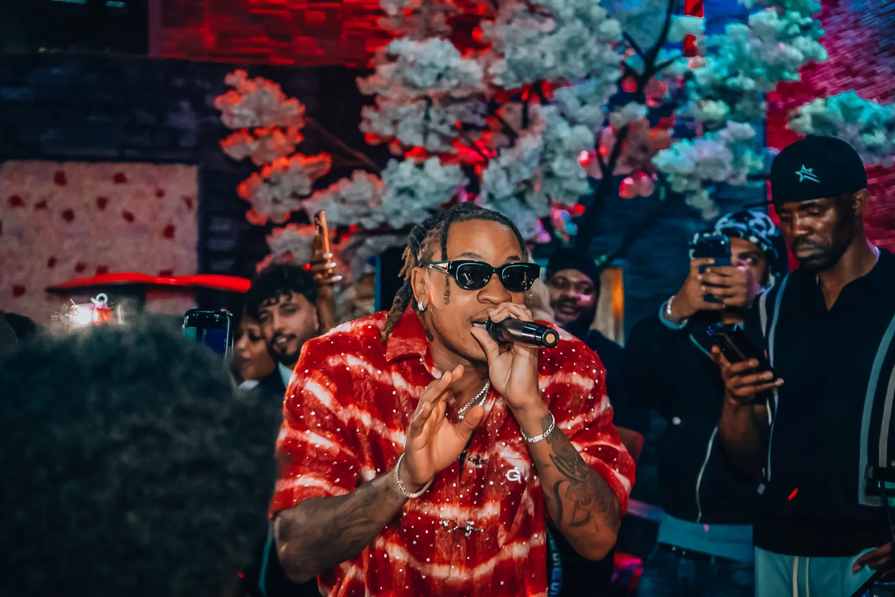 Rotimi performing in a red patterned shirt with the crowd filming him at Gate 65 in Leicester